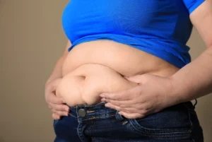 `Woman pinching stubborn belly fat before medical weight loss injections treatment in Mashpee MA`